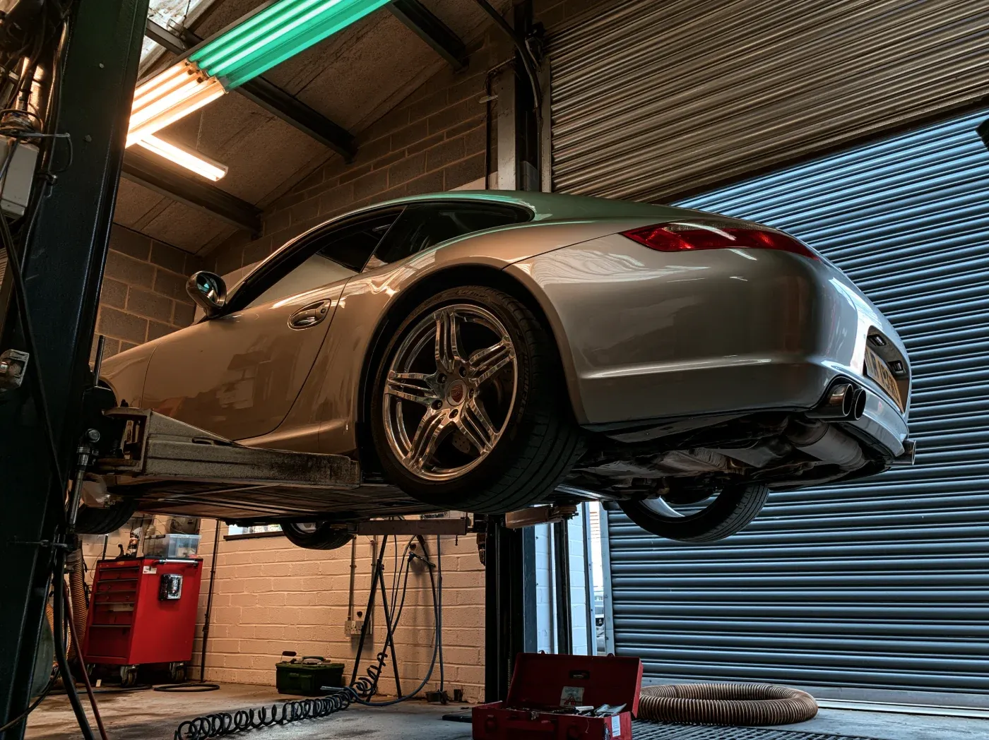A silver 997 Carrera raised on the two-post ramp mid-service
